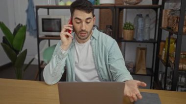 Modern ofis ortamında dizüstü bilgisayarla çalışırken telefonla konuşan genç adam, çağdaş bir iç tasarımla odaklanmış ve profesyonel bir atmosfer sergiliyor..