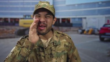 İnşaat alanında kazıcılı kamuflaj üniformalı bir adam kıt kanaat geçiniyor..