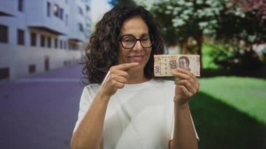 Meksika pesolarını şehir dışında elinde tutarken gülümseyen bir kadın orta yaşlı İspanyol bir kadının sokakta finansal başarılarının keyfini çıkardığını gösteriyor..