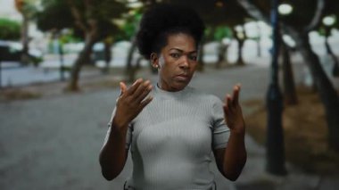 Şehirdeki genç bir kadın, elleri ağaçlarla kaplı bir caddede yelpaze gibi yüzünü sergiliyor ve doğal güzellik ve hareket yayarak canlı bir şekilde çekilen arka planı bulanıklaştırıyor..