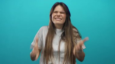 Beyaz tişörtlü İspanyol kadın, hayal kırıklığını ve kızgınlığı ifade eden gürültüye tepki olarak kulaklarını yeşil duvara yaslıyor..