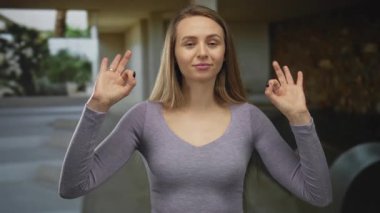 Kadın dışarıda huzurlu bir anın tadını çıkarıyor gözleri kapalı ve elleri sakin bir jestle havada, rahat bir şekilde mor bir bluz giyiyor..