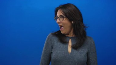 Mavi stüdyoda ağzı açık, elleri yanaklarında orta yaşlı bir kadın jest yapıyor. Sürpriz..