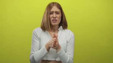 Sarışın genç bir kadın sarı bir stüdyoda kollarını göğsüne bastırıyor..