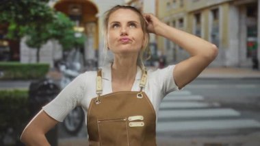 Önlüklü bir kadın, bir eli kıllı, şehir merkezinde gündüz vakti düşünceli bir şekilde ortaya çıkıyor..