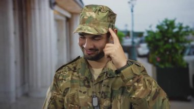 Kamuflaj üniformalı adam, şehir caddesinde künyeli, kendine güvenen birini işaret ediyor..