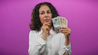 Soyutlanmış mor bir geçmişe karşı elinde İngiliz sterlinli banknotlar tutan orta yaşlı bir kadın, finansal değerlendirmeyi öneriyor..