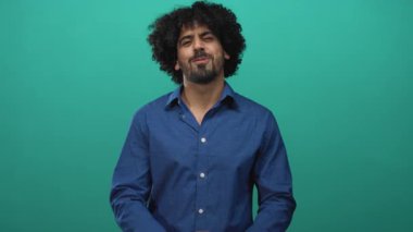 Kıvırcık saçlı, elleri mavi gömlekli, kol saati takan, göğüs göğüse hareket eden, deniz mavisi arkaplanlı bir adam..