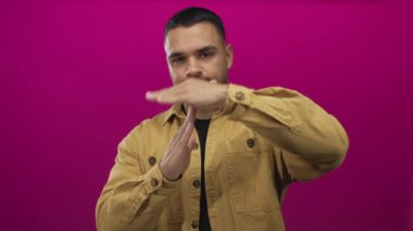 Taba rengi ceket giyen İspanyol genç adam stüdyoda canlı mor bir duvara karşı jest yapıyor..