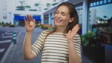 Mağazaların dışındaki mavi bir sokakta elinde ev anahtarlığı tutan beyaz bir kadın. Yeni ev heyecanı..