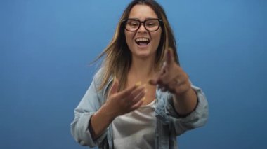 Stüdyoda eli göğsünde kamerayı işaret eden gözlüklü bir kadın..