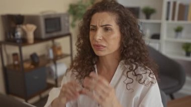 Kadın inşaat ofisinde iki eliyle başını tutuyor. Kıvırcık saçı çatık kaşlarını çerçeveliyor. Stres..