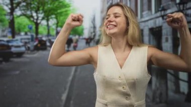 Yumrukları sıkılmış ve kolları kenetlenmiş bir kadın, park halindeki arabaların ve yeşil ağaçların yanında kaldırılmış, gülümseyerek yukarıya bakıyor; zafer sevinci..