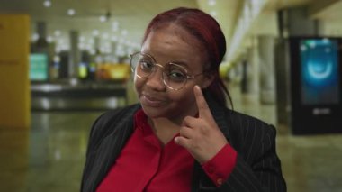 Gözlüklü ve kırmızı bluzlu bir kadın, yoğun bir havaalanı terminalinde göz göze gelir..