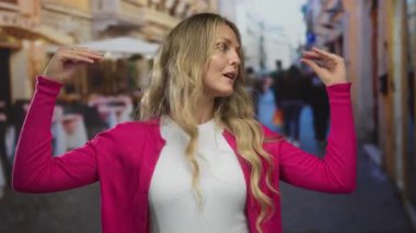 Genç bir sarışının kalabalık bir caddenin kenarındaki bir restoranın terasında konuşurken, kadın el kol hareketi yapıyor..