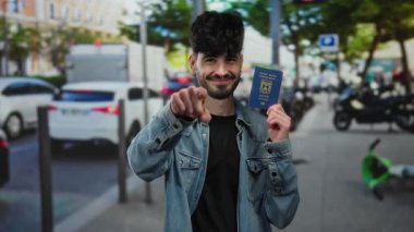 Adam, elinde İsrail pasaportu tutarken gülümsüyor ve açık gün ışığında araba ve yayalarla dolu kalabalık bir şehir sokağında jest yapıyor..