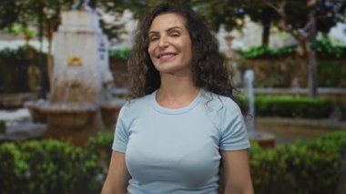 Güneş ışığı altındaki süslü çeşmenin yanındaki yeşil parkta ileri doğru işaret ederken gülümseyen kadın:.