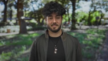 Sakallı genç İspanyol bir adam açık havada yemyeşil bir parkta benekli güneş ışığı altında doğal bir ifade ve canlı bir ortam sergiliyor.
