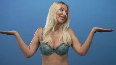 Deri dantelli sutyen giyen bir kadın, stüdyoda kollarını mavi bir duvara dayayarak poz veriyor..