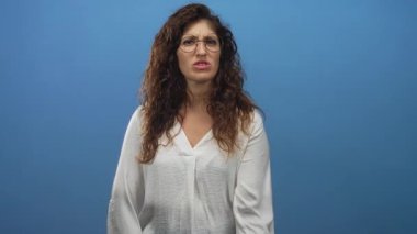 Stüdyoda el hareketi ve gergin yüz ifadesi olan bir kadın mavi arka plana karşı; can sıkıcı sabırsızlık.