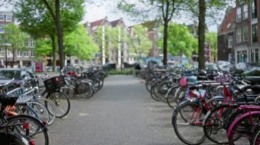 Amsterdam 'ın kentsel alanındaki ağaçların ve binaların arasındaki bulanık bisikletler şehrin canlı ulaşım kültürünü yansıtan ikonik bir bokeh görüntüsü yaratıyor..