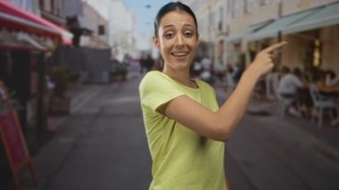 Sarı tişörtlü genç İspanyol kadın sağı işaret ediyor ve sokakta başparmak işareti yapıyor; iyimserlik onayı.