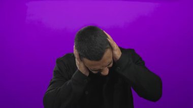 Mor stüdyodaki şiddetli gürültüye karşı adam suratını buruşturuyor ve kulaklarını kapatıyor; duyusal aşırı yüklenme sıkıntısı.
