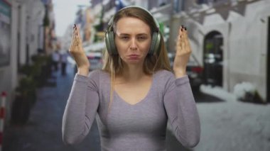 Kulaklıklı bir kadın heyecanlı şehir sokak dekorunda yüzünü kaplıyor, açık havada neşeli bir anı yakalıyor, hareketli bir şehir ortamında neşe ve sürpriz saçıyor..