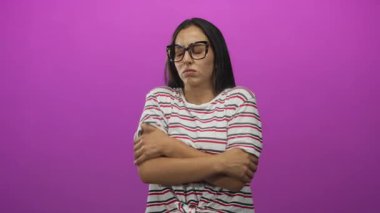 Eflatun stüdyoda çıplak omuz ve üst koluna sarılan, çizgili gömlek ve büyük gözlük takan, kapalı gözlerle irkilen bir kadın;.