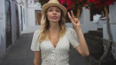 Kaldırılmış el hareketi ile parmaklarını sayan bir kadın kaldırılmış bir sokakta hasır şapka ve puantiyeli elbise giyerek; şakacı bir sayım.