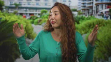 İki elini birden kaldıran bir kadın bina cephesi tarafından omuz silkme hareketi; kayıtsızlık belirsizliği.