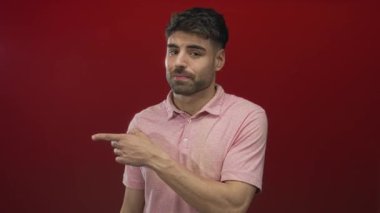 Kırmızı stüdyoyu işaret eden pembe polo tişörtlü ve gülümseyen İspanyol genç adam güven güçlendirme pozitifliği.