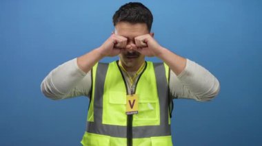 Yansıtıcı yelek giymiş genç bir İspanyol gönüllü rozeti takan, mavi arka plan duvarına göz sürtünüyor.