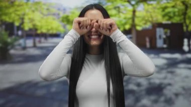 Güneşli bir şehir caddesinde elleri gözleriyle ve saçlarıyla gülümseyen neşeli açık hava neşesini yakalayan genç İspanyol kadın..