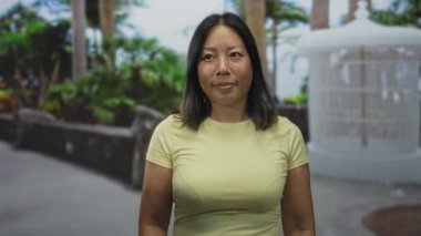 Çiçekçi ve dekoratif fıskiyenin yanında eli görünen boynuna dokunan ve saçlarını tarayan kadın, sakin yansıma.