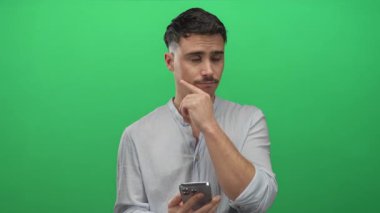 Genç adam canlı yeşil arka plan önünde akıllı telefonu tutarken, modern teknolojiyi ve içsel düşünceleri tasvir ederken, gündelik açık gömlekler giyerken,.
