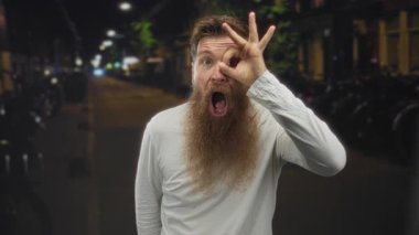 Uzun gür sakallı adam, el çerçeveli gözüyle gece loş kentsel sokağa işaret veriyor. Onaylandı..