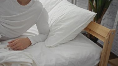 Genç adam, modern bir yatak odasında, beyaz çarşaflı, huzurlu bir şekilde uyuyor. Sakin, dinlenen ve rahatlayan bir ortam yaratıyor..