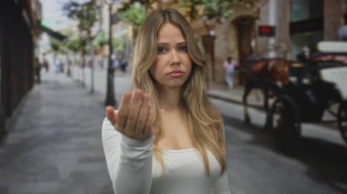 Meşgul şehir caddesinde eli beyaz bluzlu, odaklanmış ifadeye sahip sarışın kadın, sabırsızlık daveti.