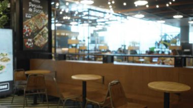 Sığ bokeh ile bulanık kafeterya arka planı ve ahşap tablolar ve sandalyeler üzerine yumuşak odak, sıcak iç aydınlatma; arka plan arka plan telif alanı sakinliği.