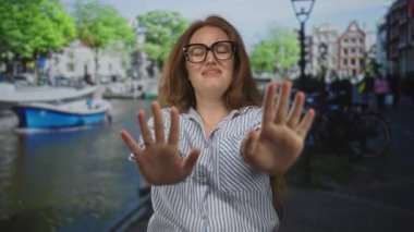 Çizgili tişörtlü kadın iki elini de kaldırıp ağaçların altındaki kanal teknesinin görüntüsünü engelliyor..