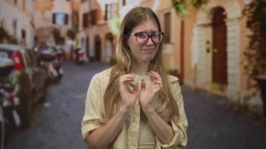 Gözlüklü sarışın kadın, gün ışığında kaldırım taşlı eski şehir sokağında parmak uçlarına dokunuyor..