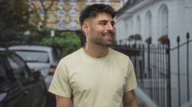 Park halindeki arabaların ve demir çitlerin yanında beyaz tişört giyen gülümseyen bir adam yüzü..