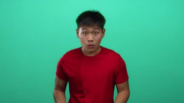 Kırmızı gömlekli genç adam yeşil arka plan üzerinde el kol hareketleri ve odaklanmış ifadesiyle kendinden emin Asyalı erkek..