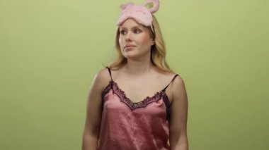 Pembe gecelikli genç sarışın kadın, sarı bir arka plana karşı şakacı çılgın bir jest yapıyor. Hoş bir ortamda eğlenceli ve kaprisli yatma anları sergiliyor..