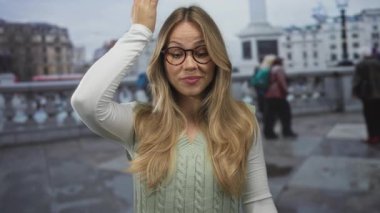 Kafkasyalı sarışın kadın Londra caddesinde şaşırmış bir şekilde kafaya dokunuyor; unutkanlık sürprizi.