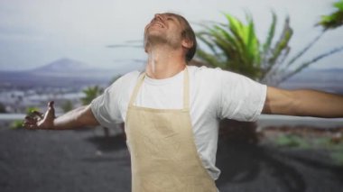 Bej renkli önlük giyen adam yemyeşil parktaki güneşli gökyüzüne doğru çıplak kollarını açar..