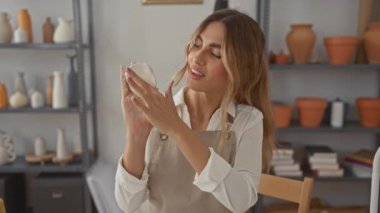 Gülümseyen sarışın kadın, parlak çömlekçilik stüdyosunda iki eliyle ıslak bir disk tutuyor..