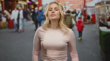 Kulaklıklı müzikten hoşlanan bir kadın hareketli bir şehir caddesinde canlı şehir atmosferini yakalayan insanlarla güven içinde duruyor..