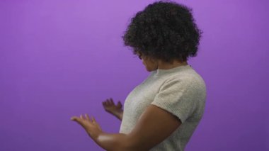 Avuç içleri açık, gülümseyen parlak bir kadın parlak mor bir stüdyoda el kol geziyor. Mutluluk..